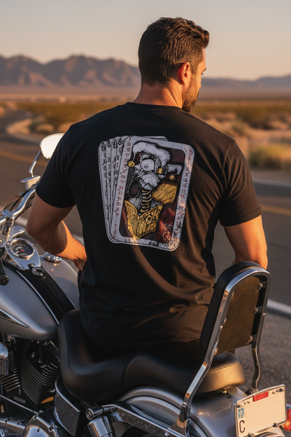 Close-up back view of Dead Man's Hand Jester Skull T-Shirt graphic — male biker leaning against a classic motorcycle on a Nevada desert roadside, men's skull biker apparel by Virginia City Motorcycle Company, VCMCo.