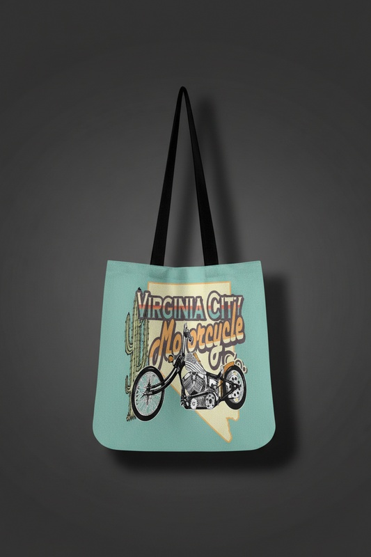 A light blue tote bag with black shoulder straps, featuring a graphic print of a vintage motorcycle, cactus, and the text 'Virginia City Motorcycle' on a dark gray background.