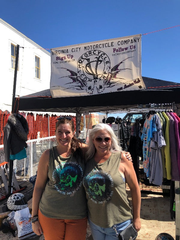 Two biker women with green skull muscle tank shirts on only by Virginia City Motorcycle Company